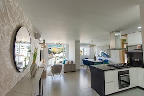 Relax in a spacious living area with a sofa, chairs, and dining table, featuring a large mirror and kitchen with a gas stove.