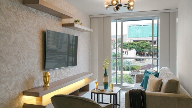 A modern living room with a flat-screen TV mounted on the wall, a sofa, a coffee table, and a view of the city through large windows. - Oasis de Lujo para descansar en Pereira (Pereira)