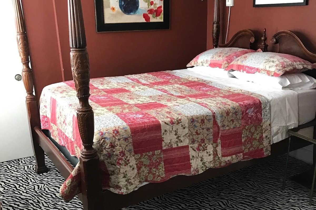 Un lit à baldaquin surmonté d’une courtepointe à motifs floraux, un tapis à rayures zébrées et deux œuvres d’art encadrées accrochées aux murs.