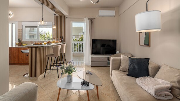A modern living room with a sofa, a coffee table, a TV, and a kitchen area with a bar. - Casa Antigone - Comfortable house in Athens Metro Mall (Athens)