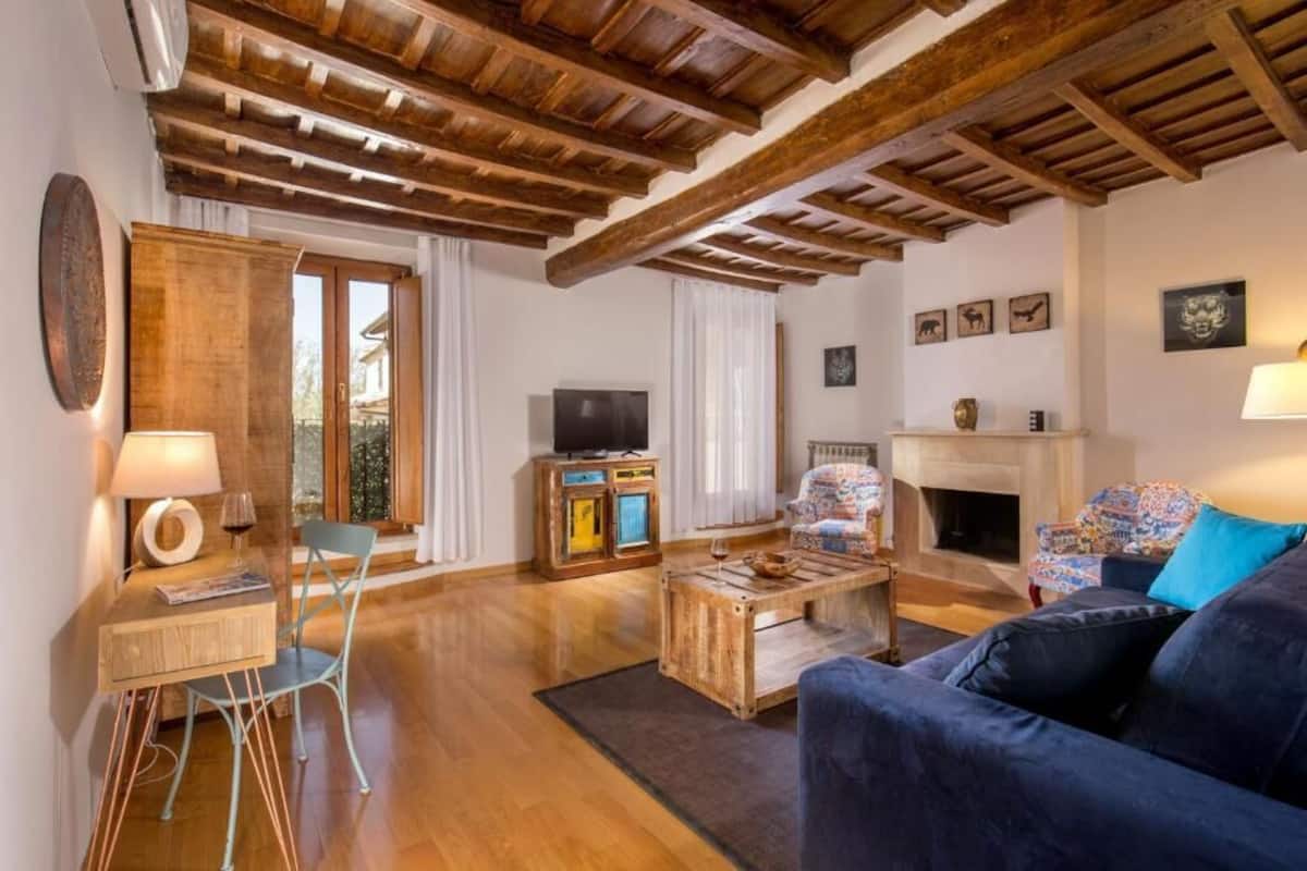 A living room with wooden beams, a television, a fireplace, and a sofa.