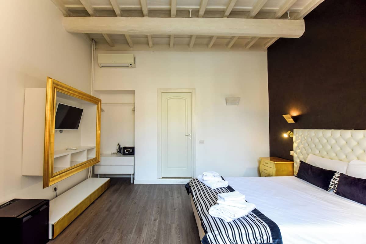 A hotel room with a bed, bedside table, TV, and a mirror.