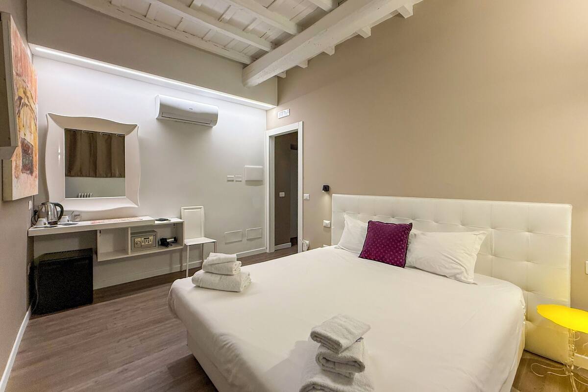 A hotel room with a large bed, a bedside table, a mirror, and a bathroom visible through an open door.