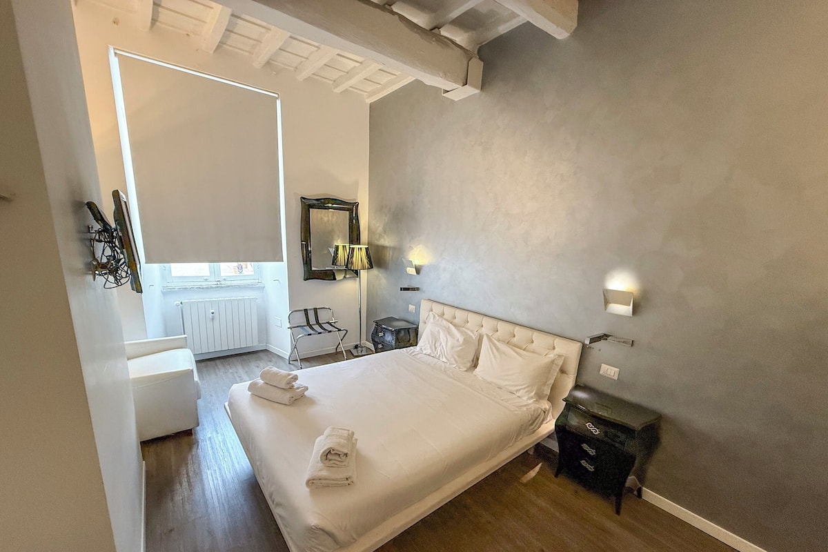 A bedroom with a large bed, bedside tables, a nightstand, a lamp, a mirror, and a window.