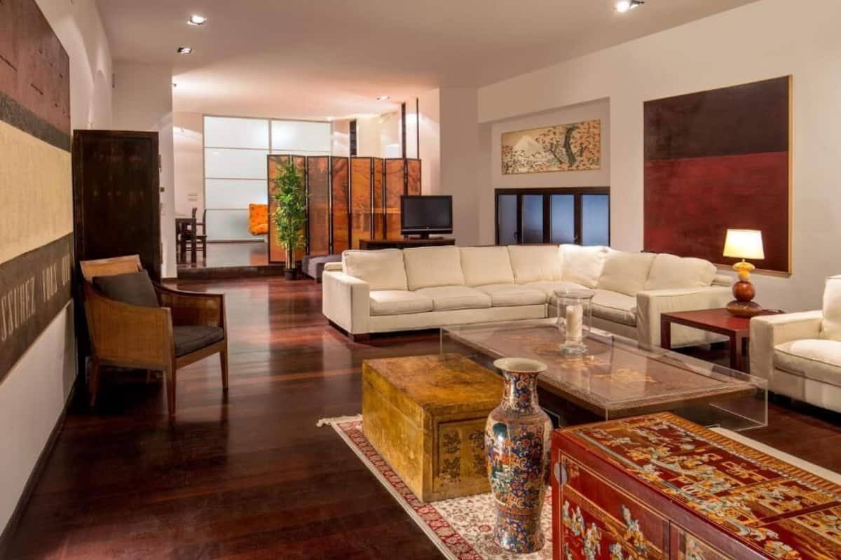 A modern living room with a white sectional sofa, a coffee table, and a traditional vase. There is a wooden cabinet and a plant in the background.
