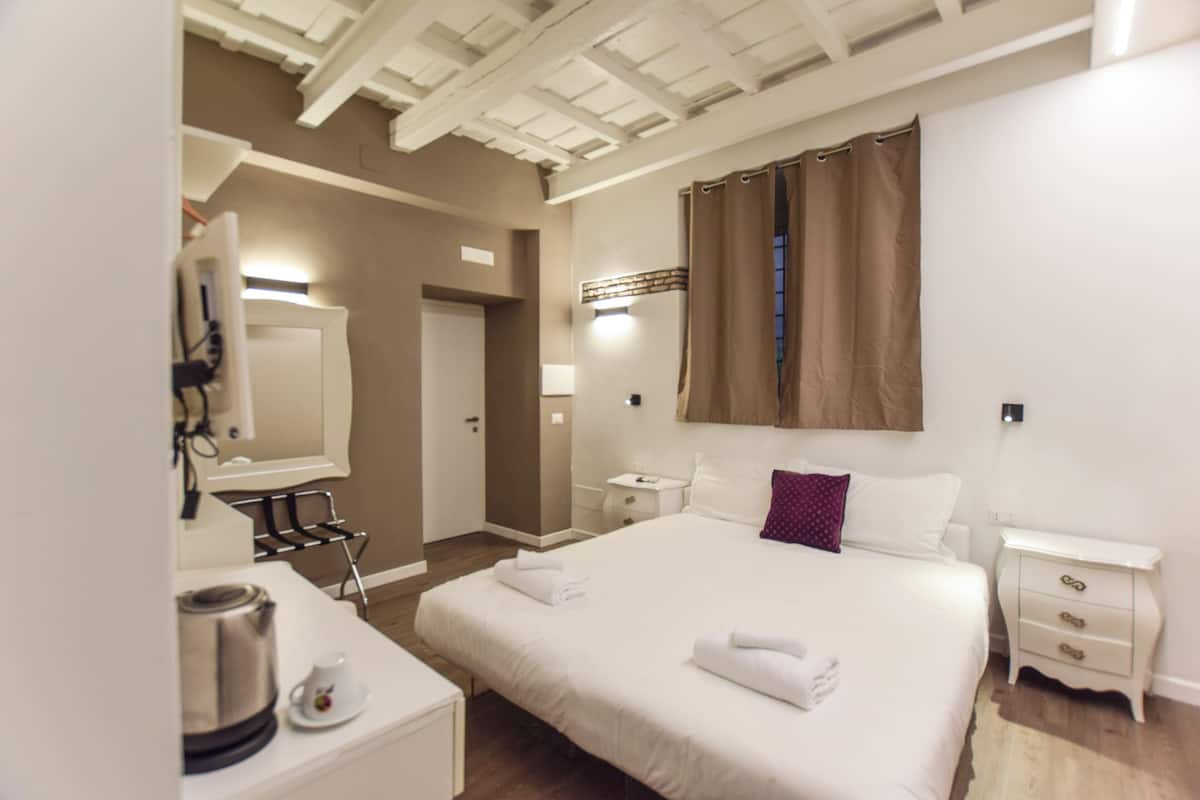 A hotel room with a bed, bedside tables, a mirror, a coffee maker, and a curtain.