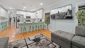 Una cocina moderna con armarios blancos, un refrigerador de acero inoxidable y un comedor con sillas verdes.