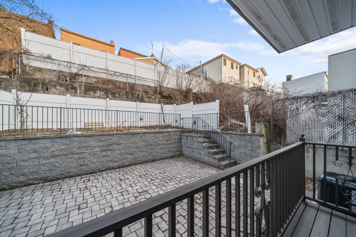 A courtyard with a stone wall, a metal fence, and a staircase leading to a higher level.