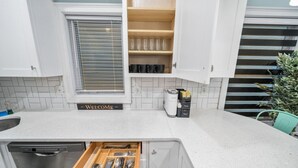 Una cocina con armarios blancos, lavavajillas integrado, cafetera y un letrero que dice 'Bienvenido'.