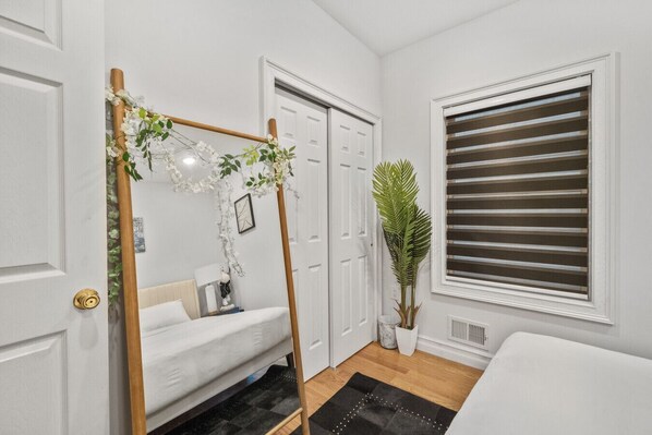 Un dormitorio con cama, un columpio de madera, una planta en maceta, una ventana con persianas y una puerta.