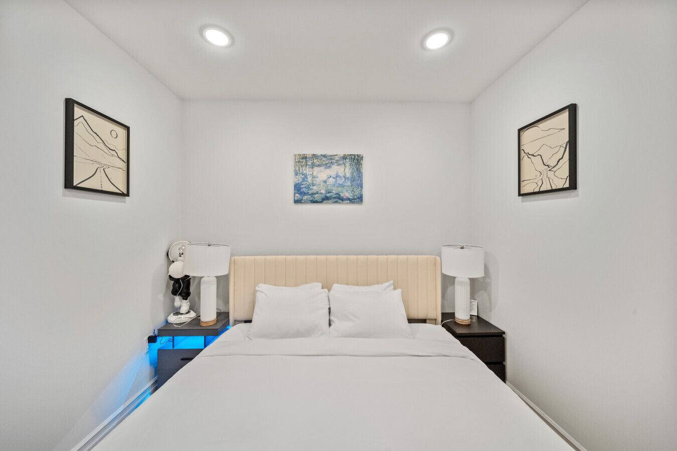 A hotel room with a bed, two bedside tables with lamps, a headboard, and three wall-mounted artworks.