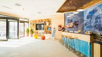 A modern hotel lobby with a reception desk, seating area, and a large wall-mounted TV.