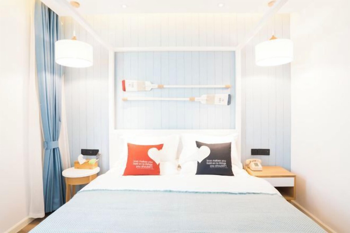 Une chambre d’hôtel équipée d’un lit, de tables de chevet, d’une petite table, d’un téléphone et d’une étagère fixée au mur.