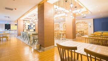A modern restaurant interior with wooden flooring, multiple dining tables, and hanging pendant lights.
