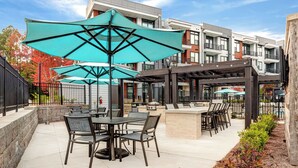 An outdoor patio area with tables and chairs, umbrellas, and a pool in the background. - Landing | Spectacular Studio, Pool, Game Room (Atlanta)