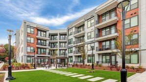 A modern multi-story residential building with balconies, a central courtyard with seating, and a well-maintained lawn. - Landing | Spectacular Studio, Pool, Game Room (Atlanta)