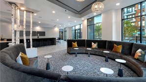 A modern lounge area with a curved sofa, small round tables, and a bar in the background. - Landing | Spectacular Studio, Pool, Game Room (Atlanta)