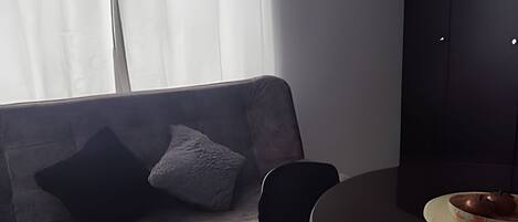 Una habitación con un sofá gris, una silla negra y una pequeña mesa redonda con un bol y un plato.