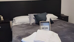 Ein ordentlich gemachtes Bett mit einem gerahmten Schild, auf dem 'In AWESOME' steht, und einem gefalteten weißen Handtuch auf dem Bett.