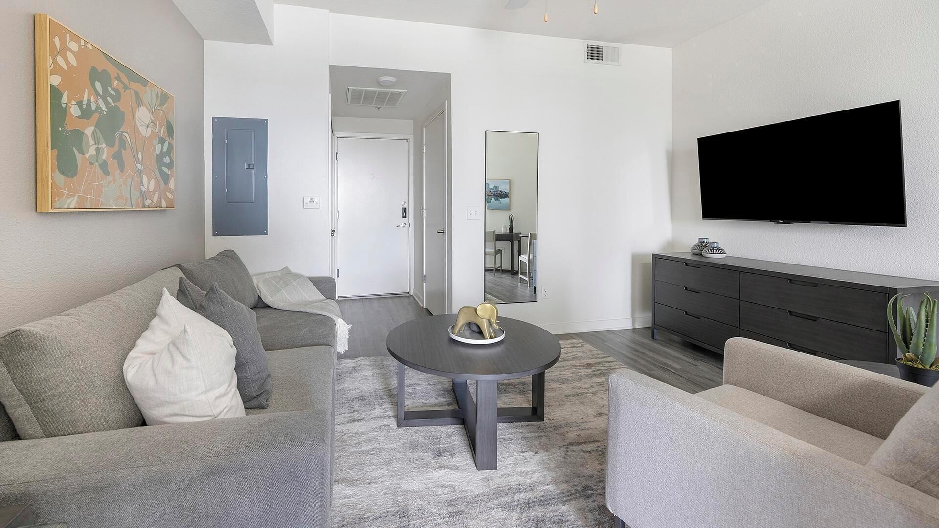 A modern living room with a grey sofa, a coffee table, a TV, and a large mirror.
