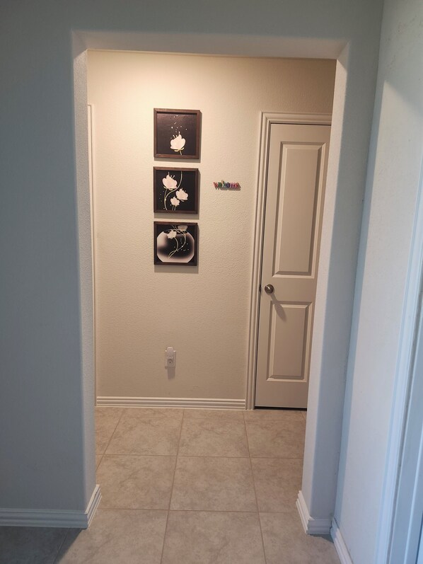 A hallway with a door, beige walls, and three framed floral artworks.