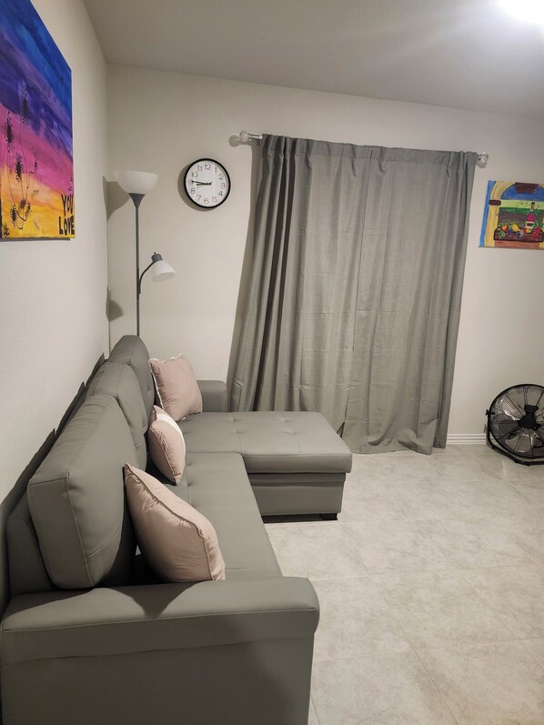 Una sala de estar con un sofá modular, un reloj de pared, una lámpara de pie y un ventilador.