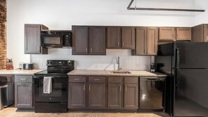 Eine moderne Küche mit dunklen Holzschränken, einem schwarzen Kühlschrank, einer Mikrowelle, einem Backofen und einem Geschirrspüler.