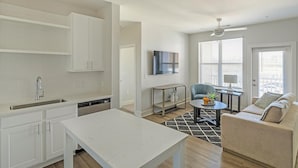 Eine moderne Küche mit weißen Schränken, einem Geschirrspüler und einem Esstisch. Es gibt einen Wohnbereich mit einer Couch, einem Couchtisch und einem Fernseher.