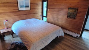 Una habitación con paneles de madera, una cama, una mesita de noche y un cuadro enmarcado en la pared.