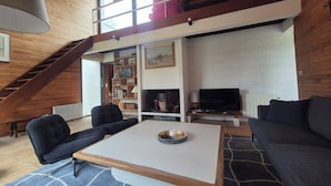 Un salón estilo loft con escaleras, chimenea, televisor y estantería.