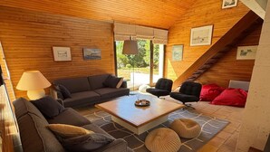 Una sala de estar acogedora, con techo de madera, un sofá, una mesa de centro y un sillón rojo.