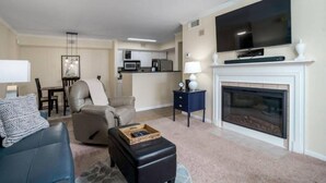 A living room with a sofa, a recliner, a coffee table, a fireplace, a television, and a kitchen in the background. - Beach short drive - Pool - Hot Tub K/Q, 2 BA, Sleeps 4 in beds- Ground Floor (Gulf Shores)