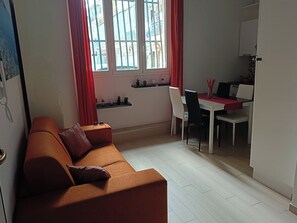 A compact living space with a sofa, a dining table with chairs, a kitchen area, and a window with curtains. - Beautiful loft (for 3 people) in Catania, available for short-term rentals (Catania)