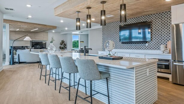 Een moderne keuken met een centraal eiland, barkrukken, een grote televisie en roestvrijstalen apparatuur.