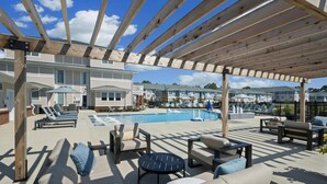 Een overdekt buitenzwembad met ligbedden en een jacuzzi, omgeven door een houten pergola.