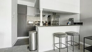A compact kitchen with a central island, stainless steel appliances, and a trash can. - Landing | Beautiful Studio, Gym, Pool (Winston-Salem)