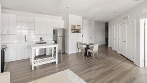 A modern kitchen with white cabinetry, a built-in oven, and a dining area with a round table and two chairs. - Landing | Chic 1BD, Courtyard, Yoga Studio (Huntsville)