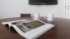 A round table with a magazine, two white mugs with Italianway logos, and a black TV on the wall. - Italianway Comfort - Copernico 47 B (Milan)