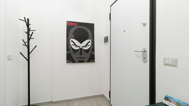 A hallway with a coat rack, a door with a light switch, and a poster on the wall. - Italianway Comfort - Copernico 47 B (Milan)