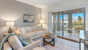 A modern living room with a sofa, armchair, and coffee table, a painting on the wall, and a balcony with a view. - Landing | Stunning 1BD, Gym (North Las Vegas)