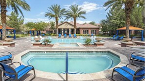 A pool area with lounge chairs, palm trees, and a building with a tiled roof. - Landing | Stunning 1BD, Gym (North Las Vegas)