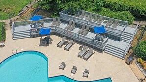 Un espace piscine aménagé sur le toit, avec des chaises longues et des parasols, entouré d’une terrasse en bois et d’une piscine.