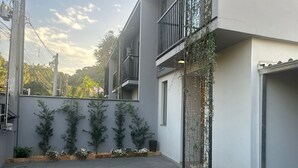 A modern building with a balcony, a small garden area with potted plants, and a concrete ground. - GEMINADO CASA 2 ALTO PADRÃO 3 QUARTOS (Joinville)