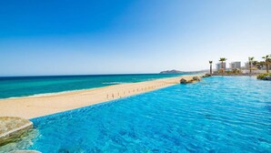Vista de la piscina con playa y océano, bajo un cielo despejado.