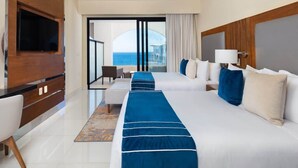 Habitación de hotel con dos camas, televisión, ventilador de techo y vista al mar.