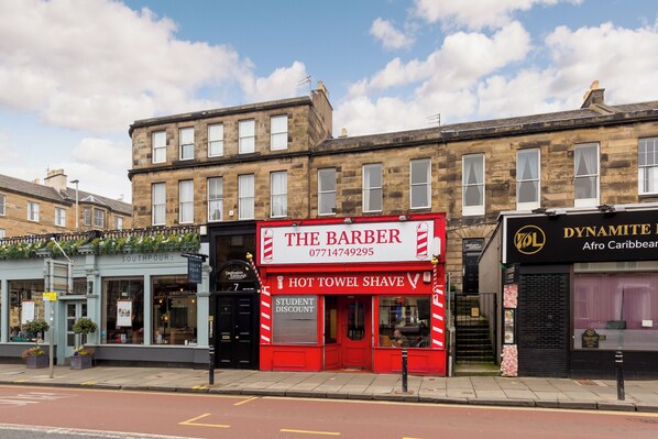 Une vue d’une rue où l’on aperçoit un salon de coiffure appelé « The Barber » et un restaurant appelé « Dynamite Afro Caribbean ».