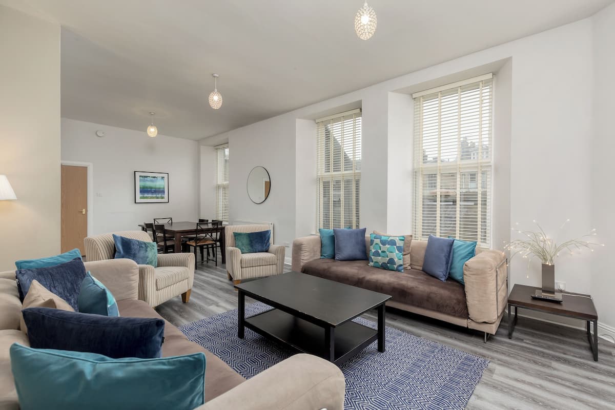 A modern living room with a sofa, armchairs, a coffee table, and a dining area.
