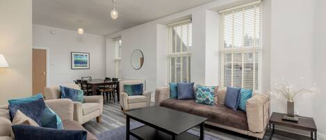 A modern living room with a sofa, armchairs, a coffee table, and a dining area.