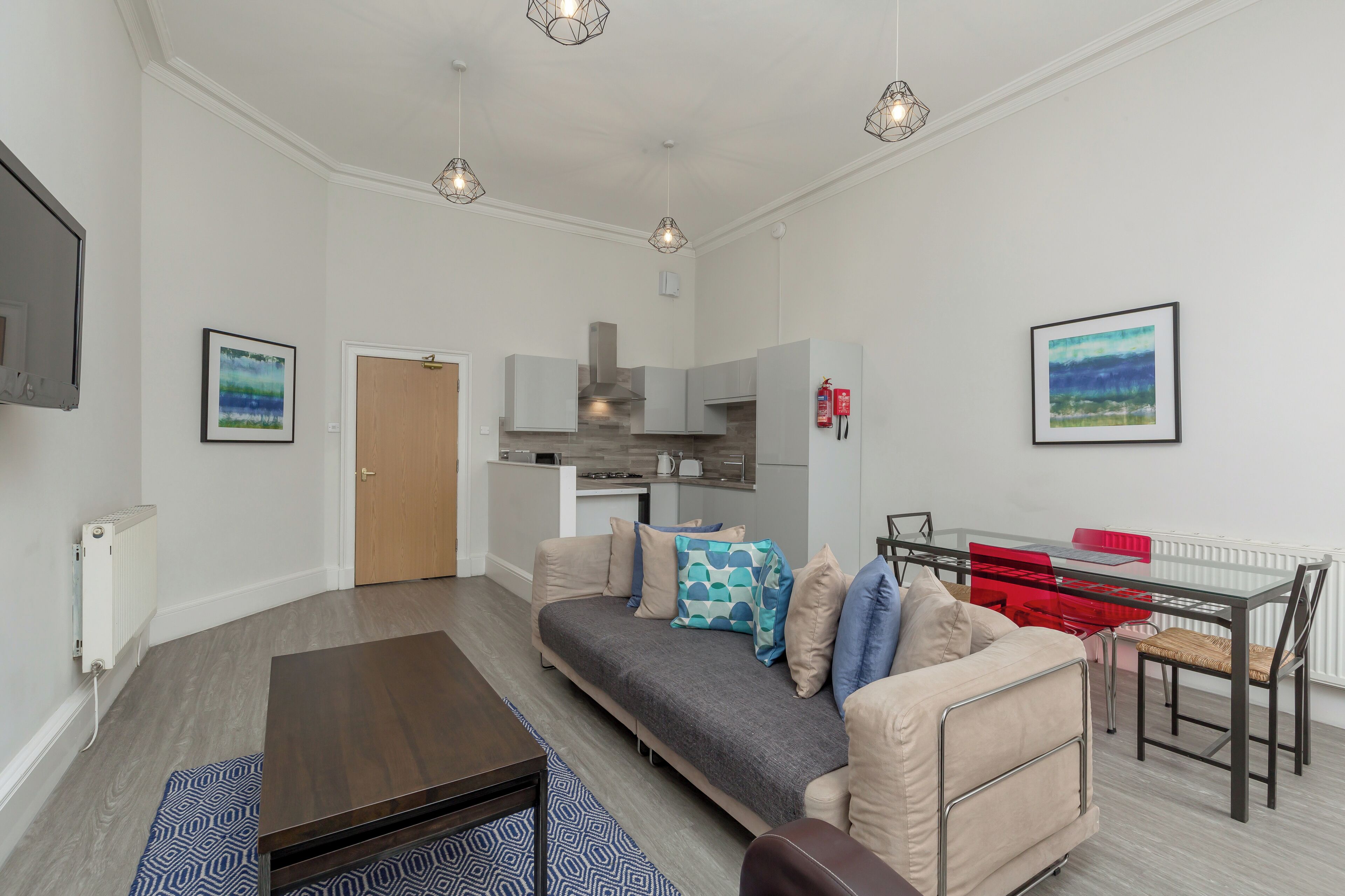 Een moderne woonkamer met een bank, een glazen eettafel en een keuken op de achtergrond.