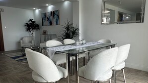 Un comedor moderno con una mesa de vidrio, sillas blancas con tapicería y un suelo de madera con diseño en espiga.